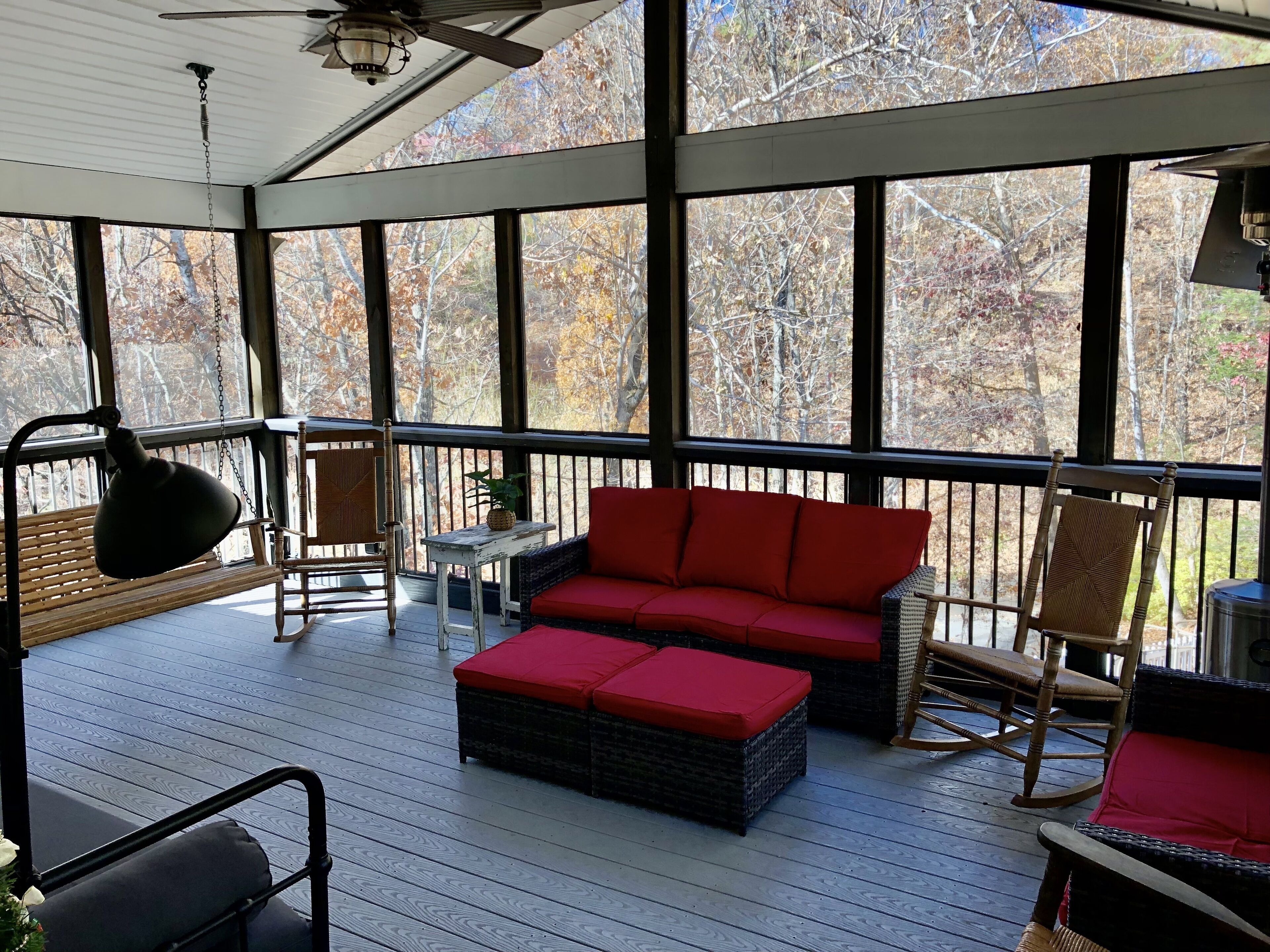 A covered porch with a red sofa, wicker chairs, and a ceiling fan.
