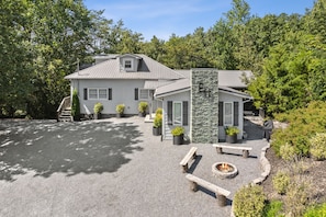 A two-story house with a stone facade, a fire pit, and a bench.