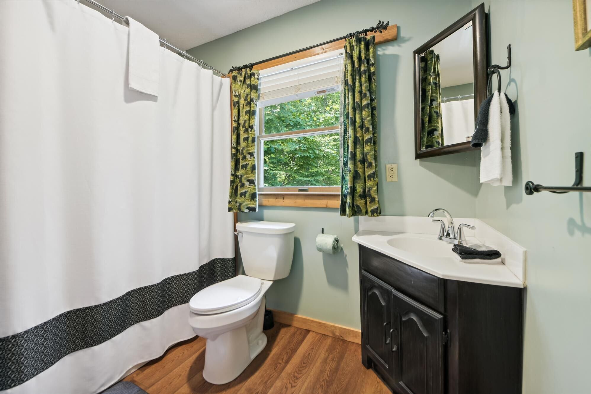 Une salle de bain avec des toilettes, un lavabo et une fenêtre avec des rideaux.