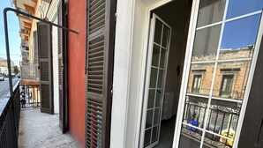 Un balcone con ringhiera metallica, una porta scorrevole in vetro e vista su una strada con auto parcheggiate.
