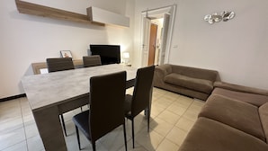 Un soggiorno moderno con un divano beige, un tavolo da pranzo con sedie e una zona cucina con televisore e lampada.