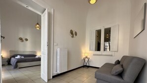 Un soggiorno moderno con un divano grigio, un letto con biancheria da letto grigia, un termosifone e una finestra con vista.