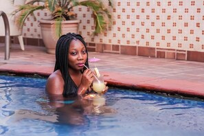 Une personne dans une piscine, tenant un verre avec une paille et un petit parasol.