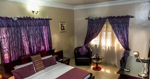 A hotel room with a bed, a chair, a desk, and curtains. - Apartment Royale Hotel and Suite (Lagos)