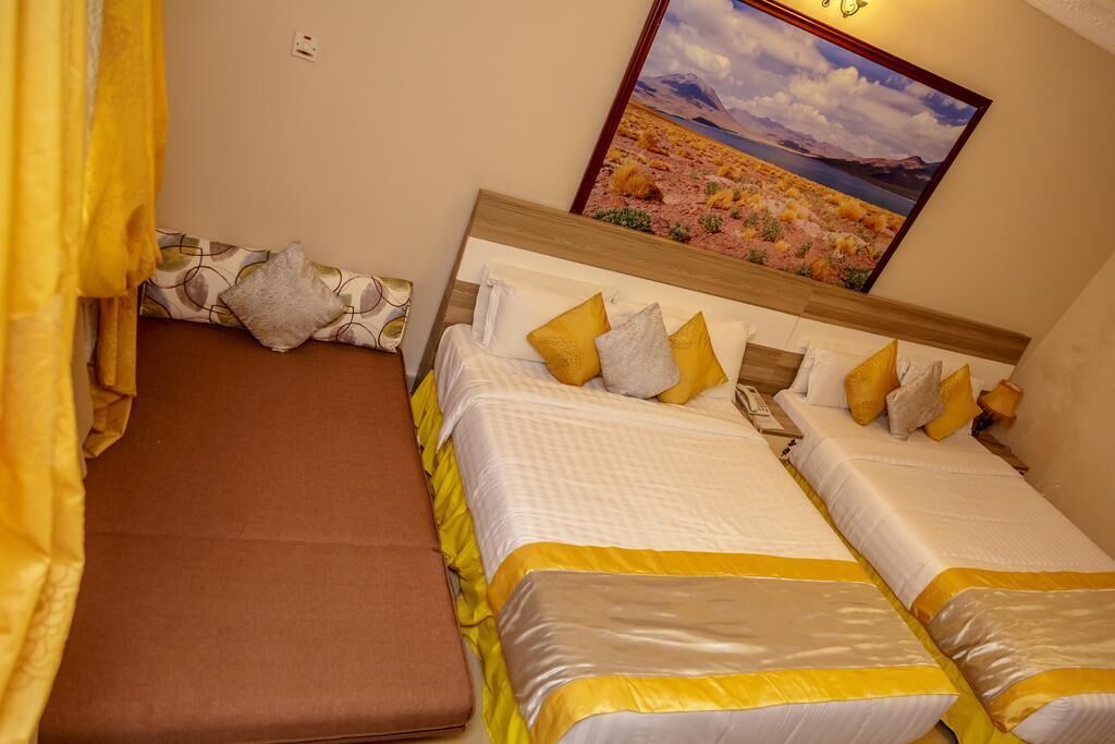 A hotel room with two beds, a brown bench, and a painting of a desert landscape.