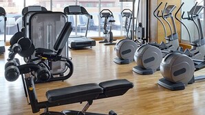 Een fitnessruimte met diverse trainingsapparaten, een bank en een groot raam met uitzicht op buiten.