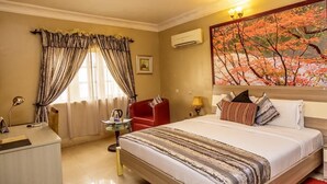 Een hotelkamer met een groot bed, een bureau, een stoel, een raam met gordijnen en een schilderij aan de muur.