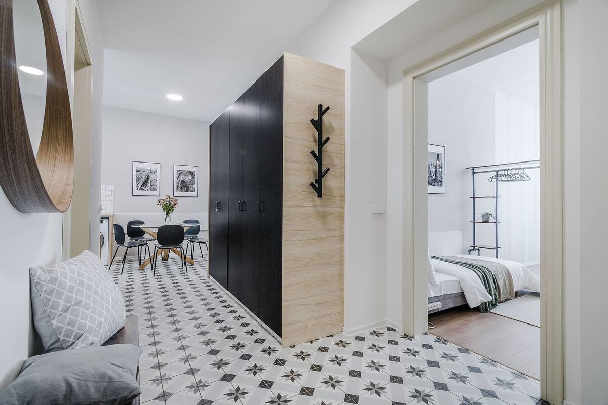 Ein modernes Hotelzimmer mit einem großen Bett, einer Sitzecke inklusive Sofa und Sesseln, einem Esstisch mit Stühlen und einem Flur mit einer Holzvertäfelung und einem schwarzen Kleiderständer.