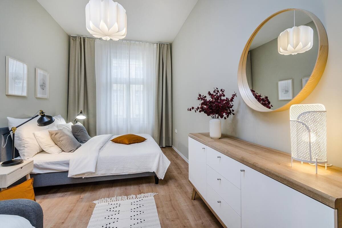Ein modernes Schlafzimmer mit Bett, Nachttischlampen, einem Schminktisch, einem Spiegel und einer Dekovase.