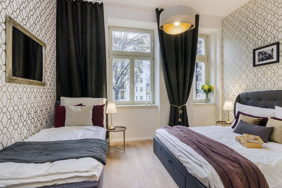 Ein Hotelzimmer mit zwei Betten, einem Fenster mit Vorhängen, einem Nachttisch mit Lampe und einem gerahmten Bild an der Wand.