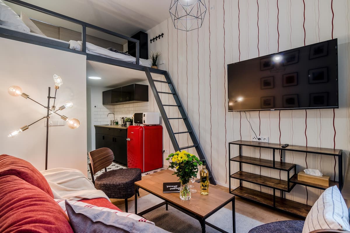 Ein modernes Loftzimmer mit Etagenbett, einem Essbereich mit Holztisch, einem roten Kühlschrank und einer Küche im Hintergrund.
