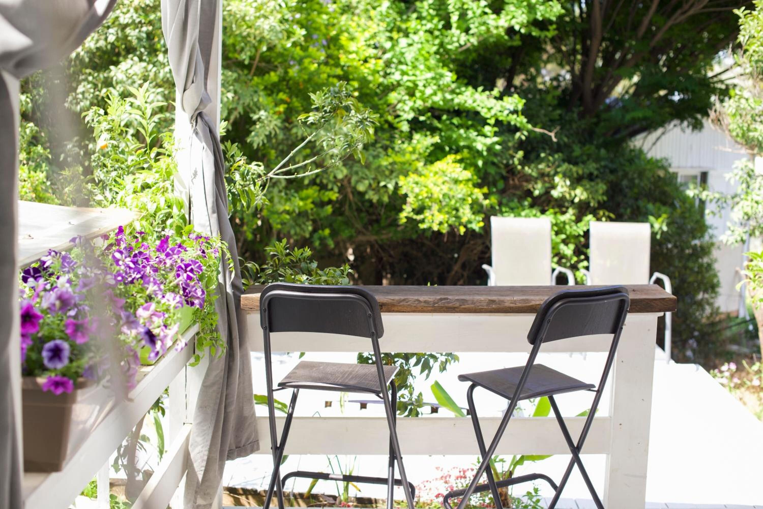 Un patio con dos sillas negras, una mesa de madera y una barandilla blanca.