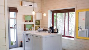 A compact kitchen with a central island, a refrigerator, and a window with a view of greenery. - Eili Suites (Ramot)