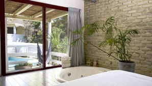 A bedroom with a large window, a bathtub, and a potted plant. - Eili Suites (Ramot)