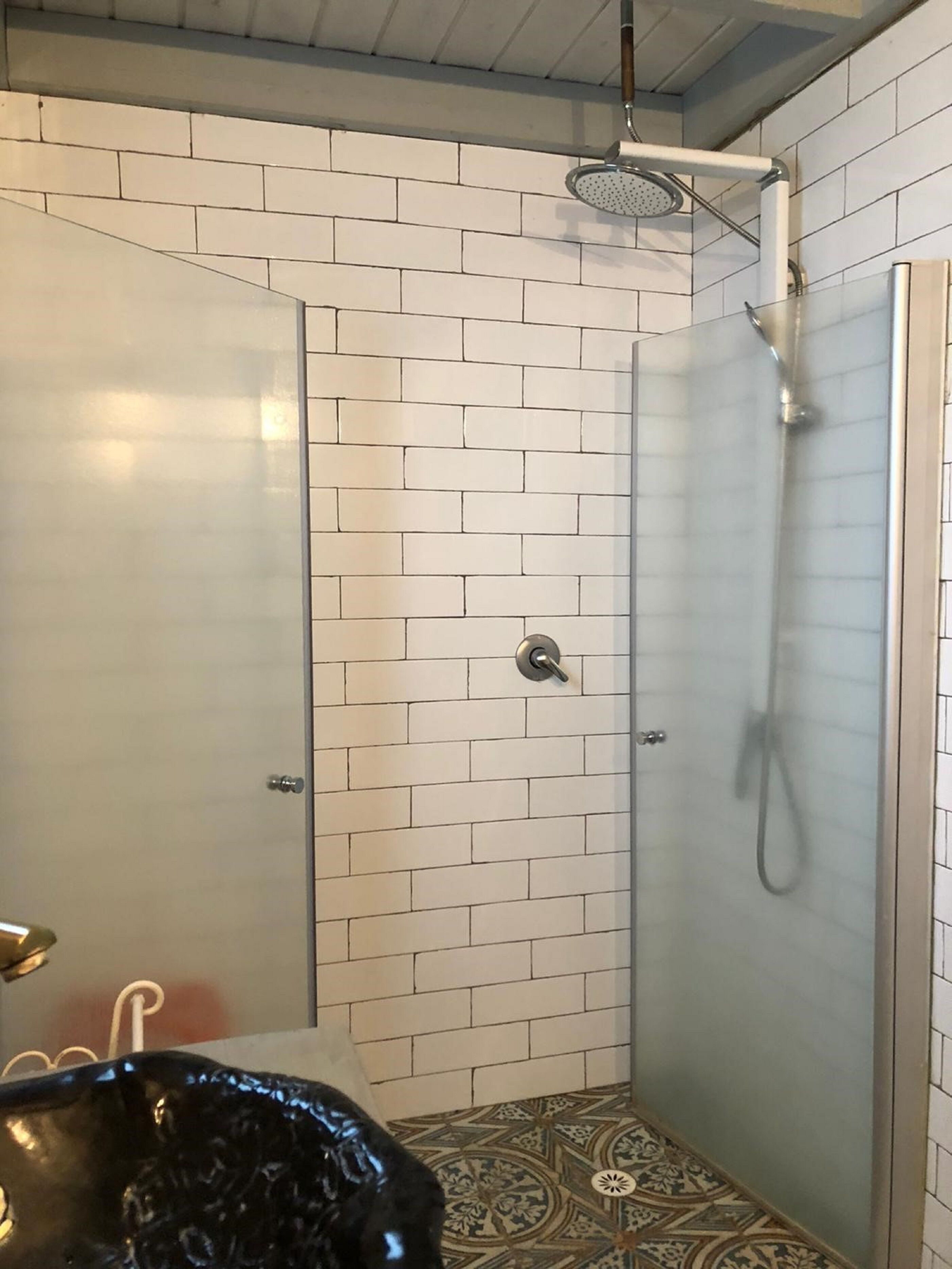 Una ducha con puerta de vidrio, paredes cubiertas de azulejos blancos y piso con diseño.