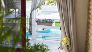 A pool area with a white deck, a planter with purple flowers, and a view of a white fence and greenery outside. - Eili Suites (Ramot)