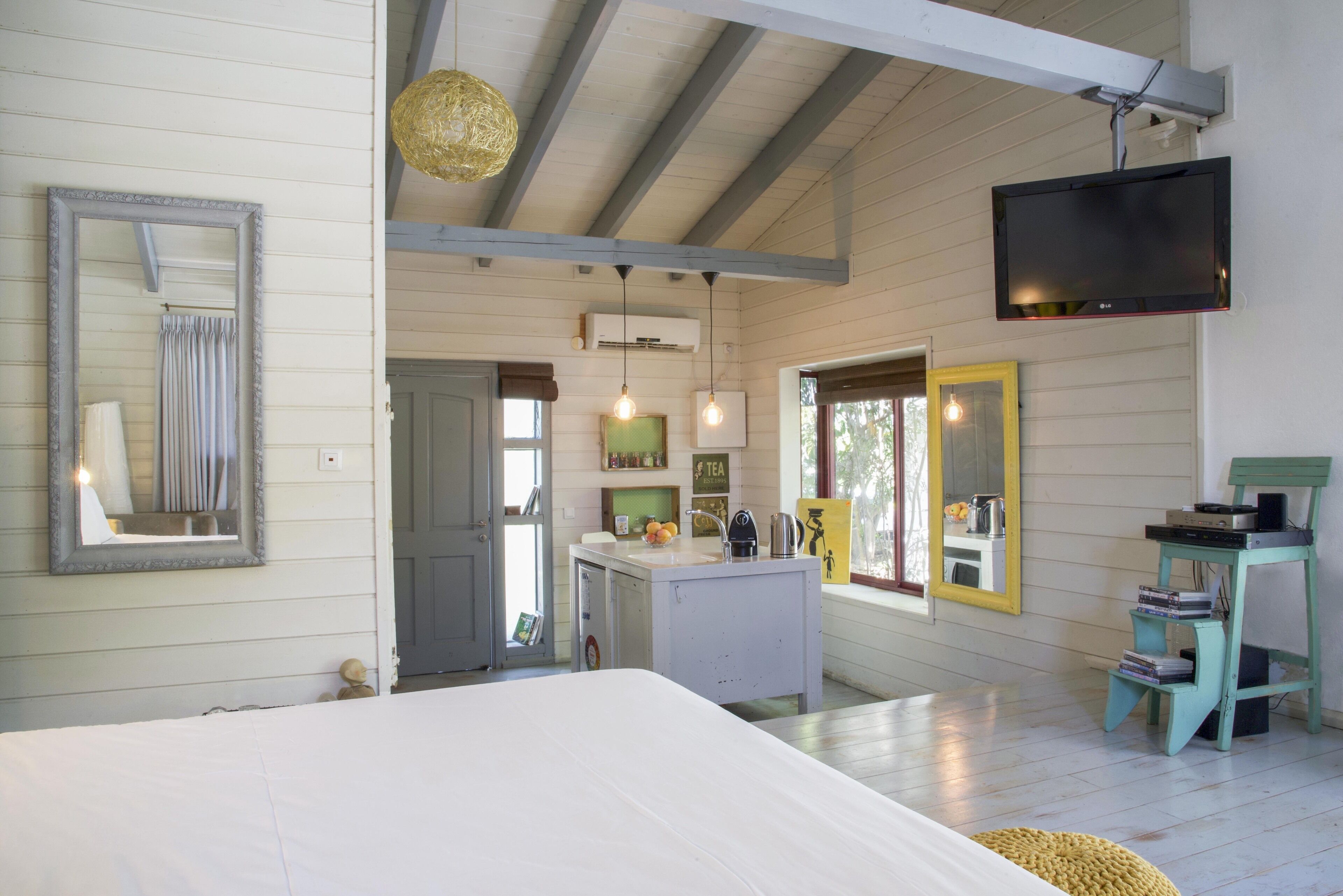 A bedroom with a large bed, a TV mounted on the wall, and a kitchenette area with a sink and countertop.
