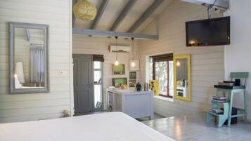 A bedroom with a large bed, a TV mounted on the wall, and a kitchenette area with a sink and countertop.