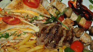 Un piatto con bistecca alla griglia, patatine fritte, un panino e verdure grigliate.