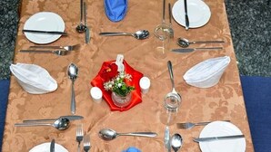 Tavolo quadrato apparecchiato per quattro persone, con piatti bianchi, posate e tovagliolo rosso con composizione floreale.