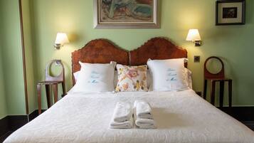 Una cama bien hecha con sábanas blancas y dos almohadas, un par de toallas dobladas y dos lámparas fijadas a la pared.