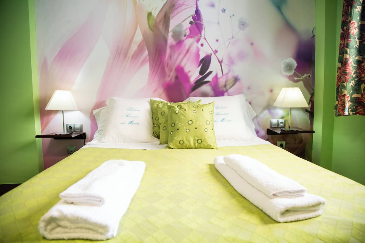 A hotel room with a bed, green walls, floral wallpaper, two bedside lamps, and a green pillow.