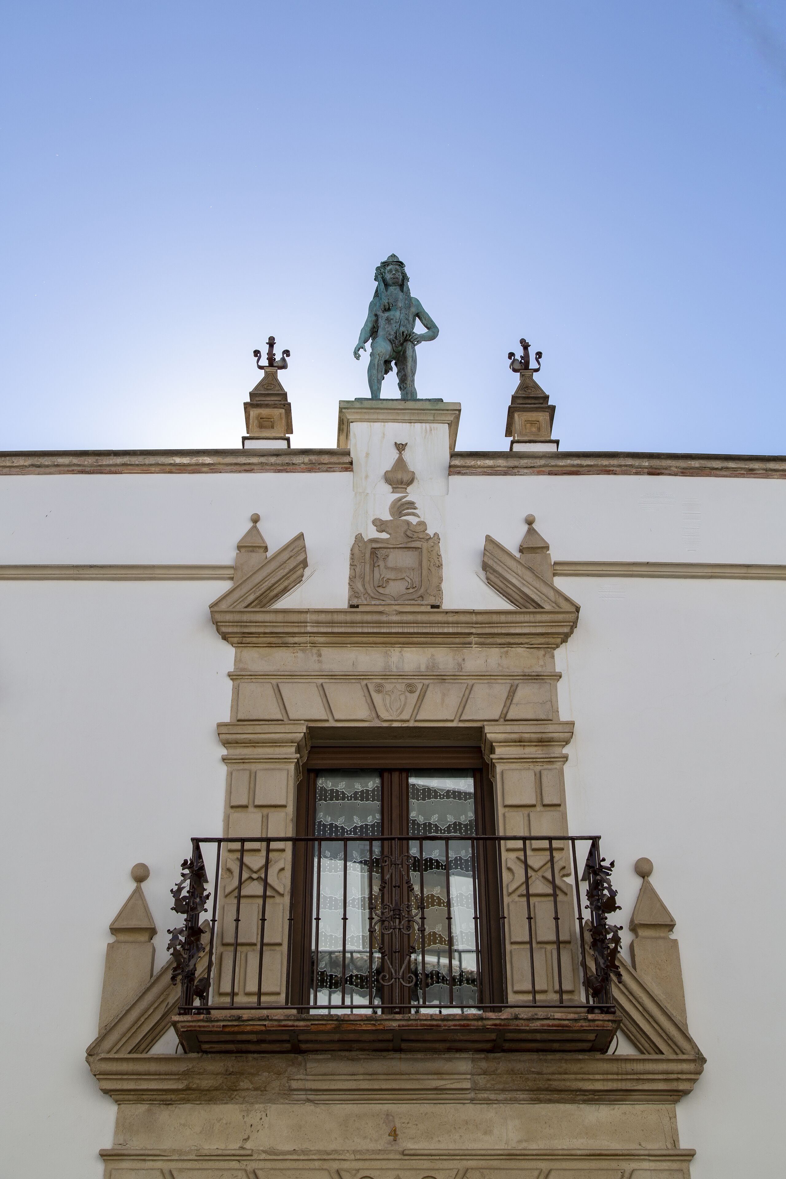 Fachada de edificio con una estatua central, barandillas de balcón ornamentales y una ventana decorativa.