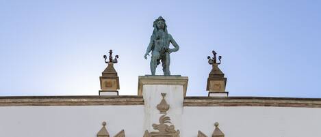 Fachada de edificio con una estatua central, barandillas de balcón ornamentales y una ventana decorativa.