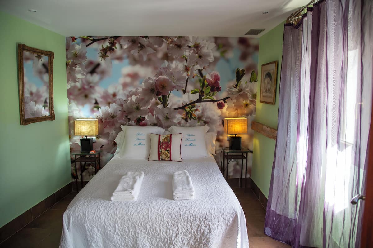 A hotel room with a large bed, floral wall art, two bedside lamps, and a window with curtains.