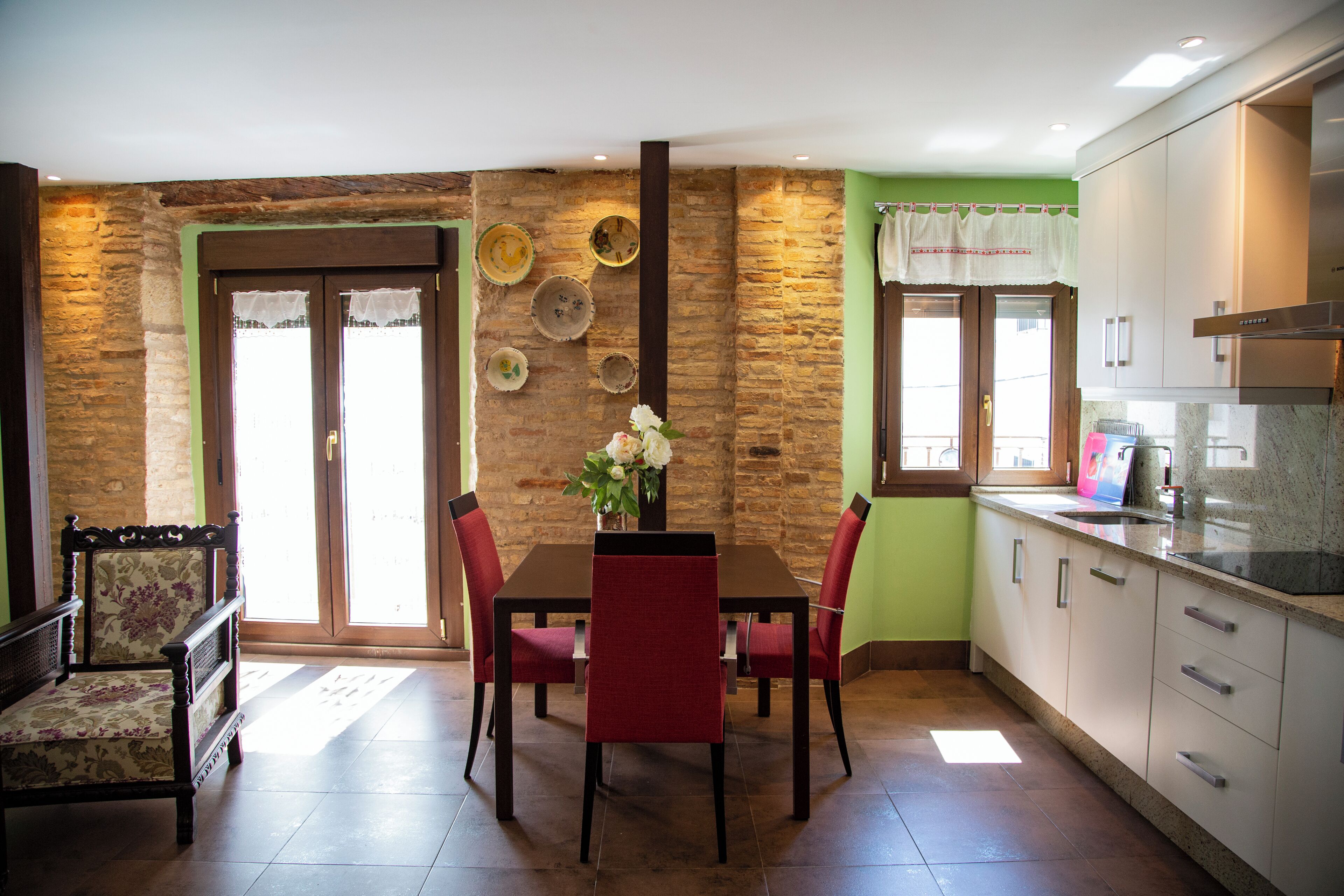 Un comedor con una mesa y sillas de madera, un florero con flores y una pared de piedra.