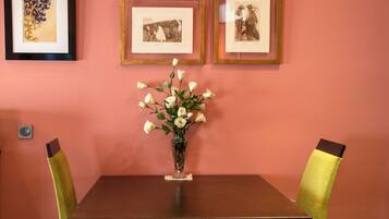 A dining area with a table, chairs, and a vase of flowers. There are framed pictures on the wall.
