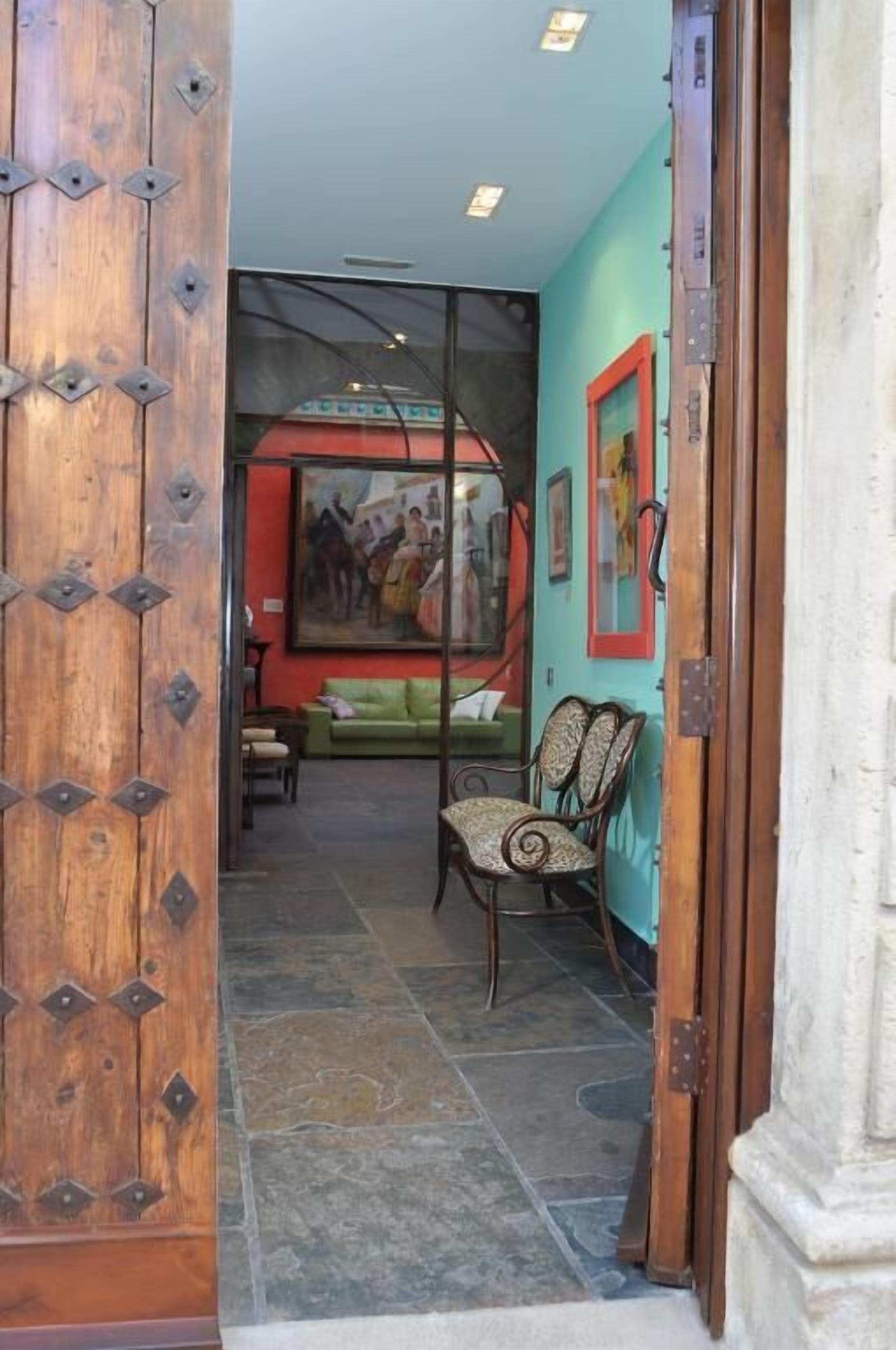 Une pièce avec une porte en bois, un canapé vert, un fauteuil à motifs et un tableau accroché au mur.