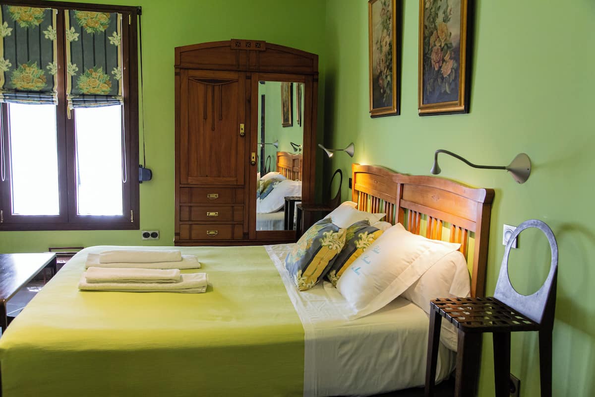 A neatly made bed with a green bedspread, a wooden headboard, and a bedside table with a lamp.