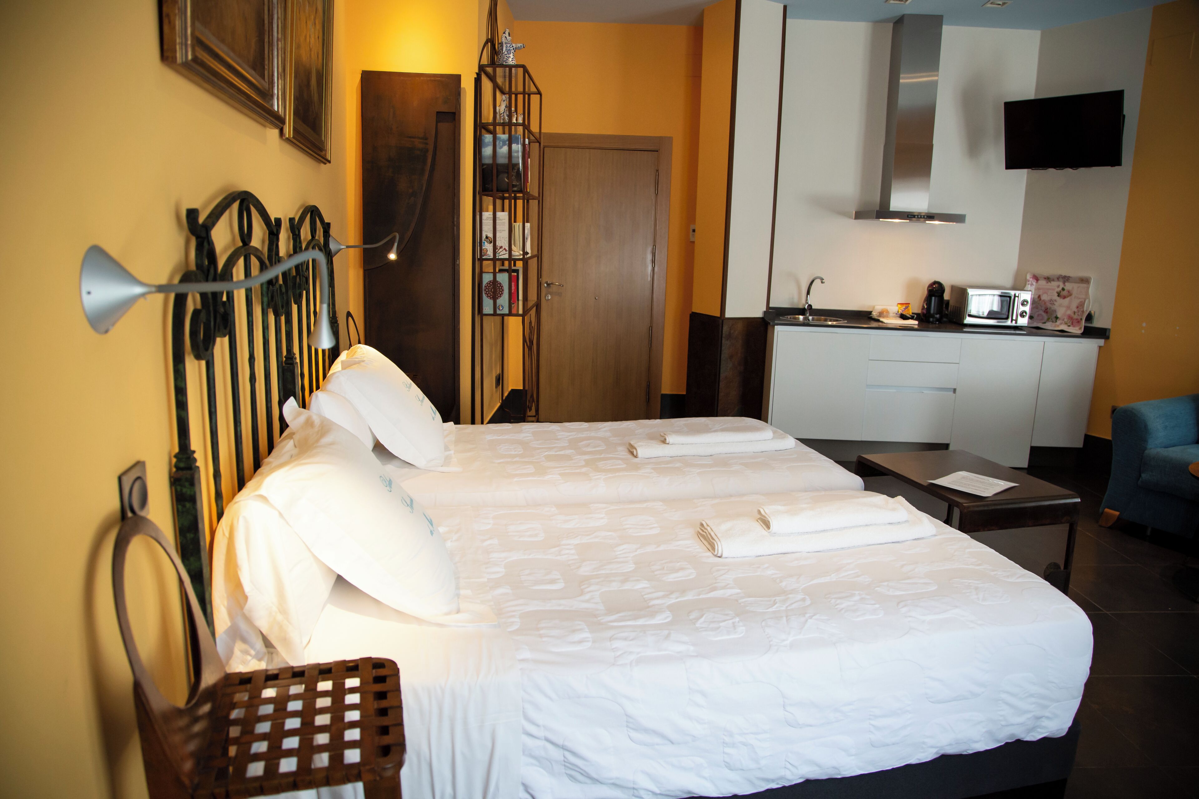 A hotel room with a large bed, a desk, a chair, a bookshelf, and a kitchenette.
