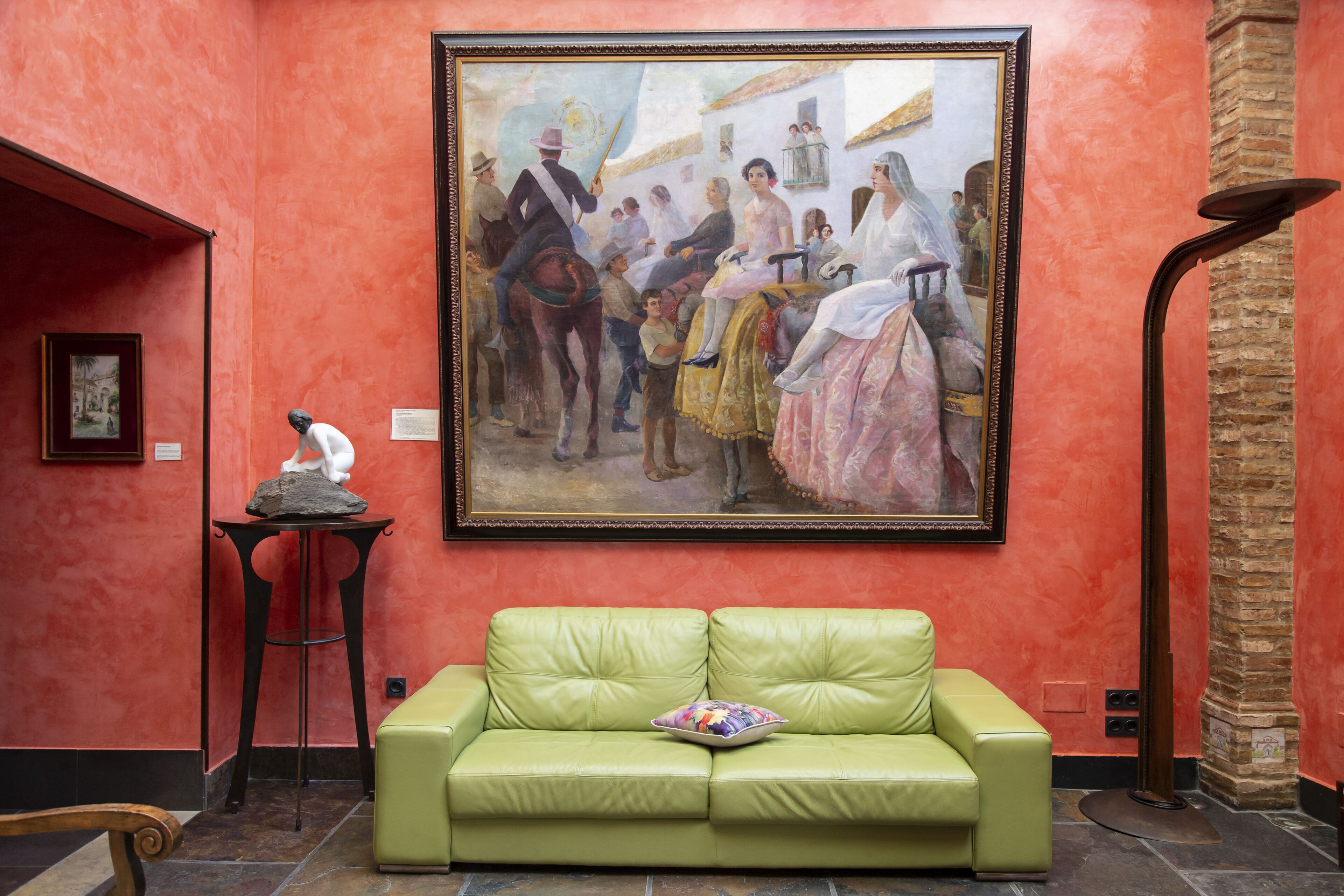 A room with a green leather sofa, a framed painting on the wall, and a small table with a sculpture.