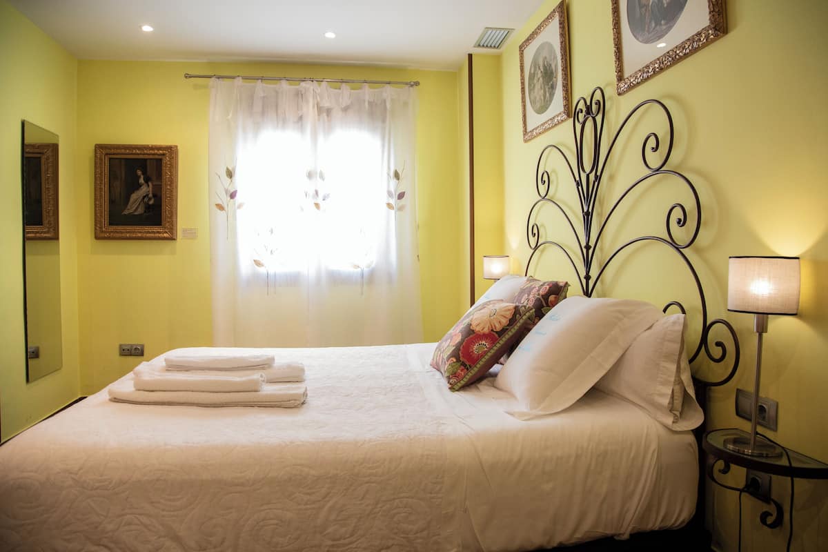 A neatly made bed with folded towels, a decorative pillow, and a bedside table with a lamp.