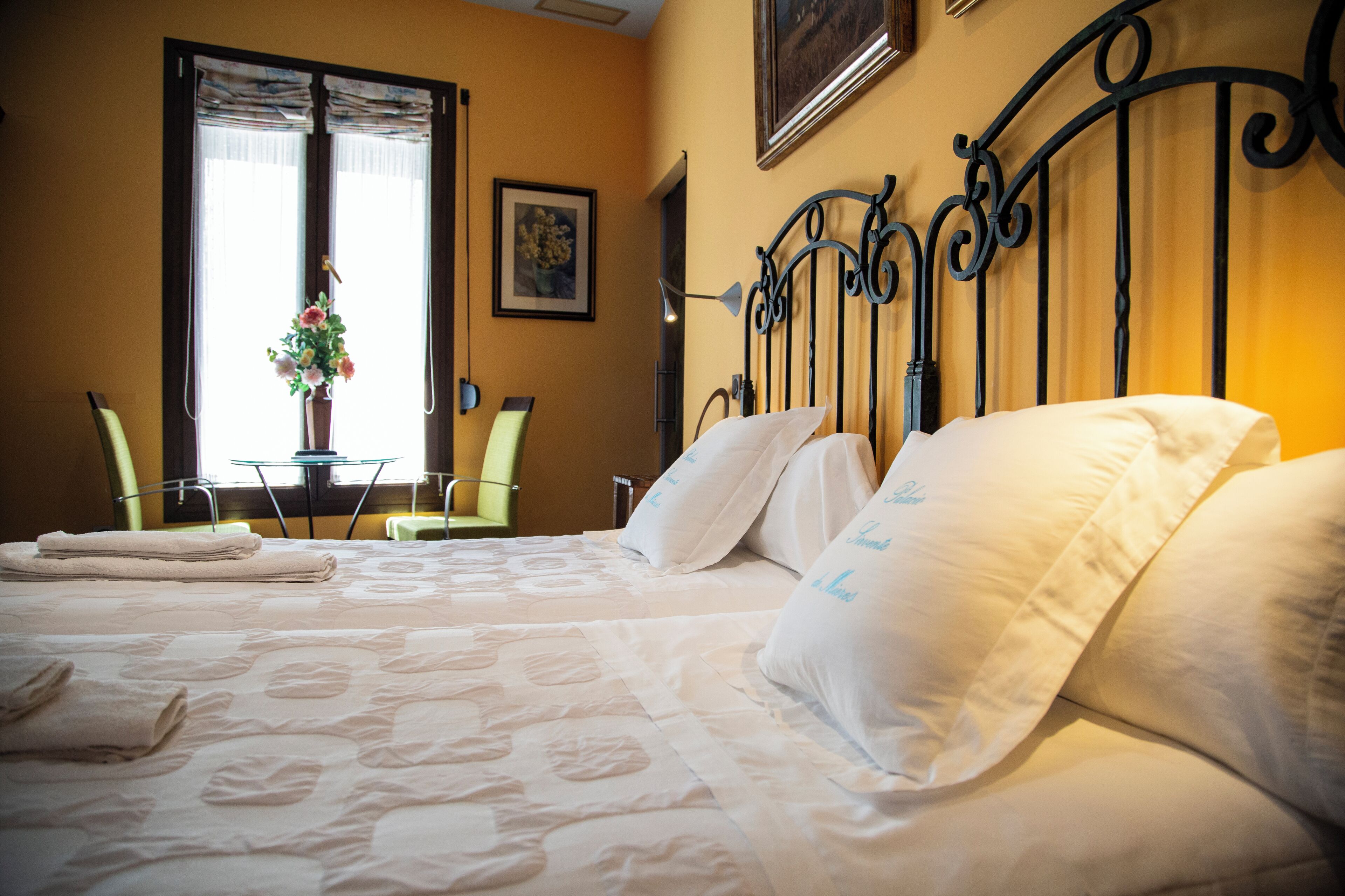 Habitación de hotel con dos camas, una zona de estar con mesa y sillas, y una ventana con cortinas.