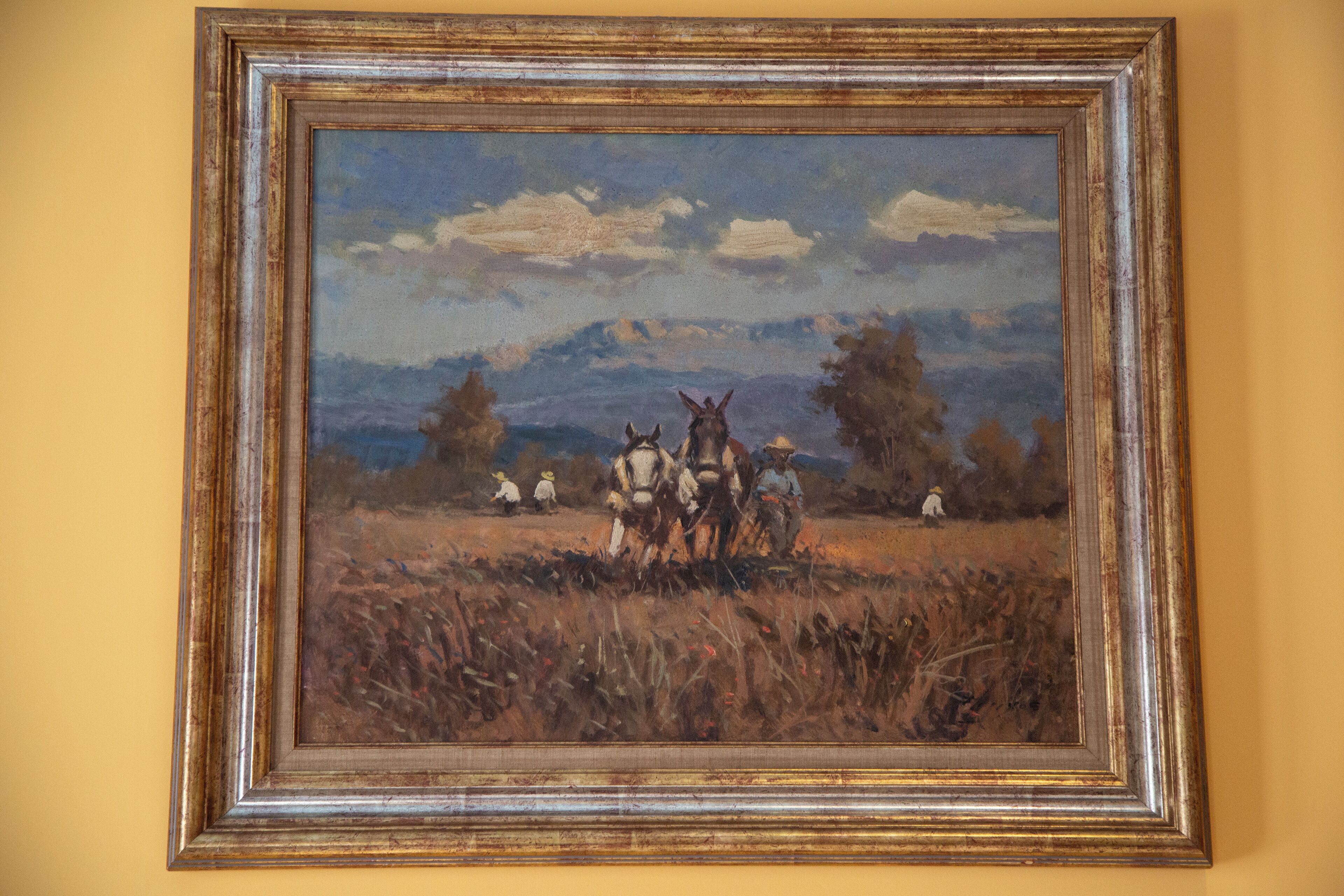 Un cuadro enmarco de un paisaje con caballos y personas.
