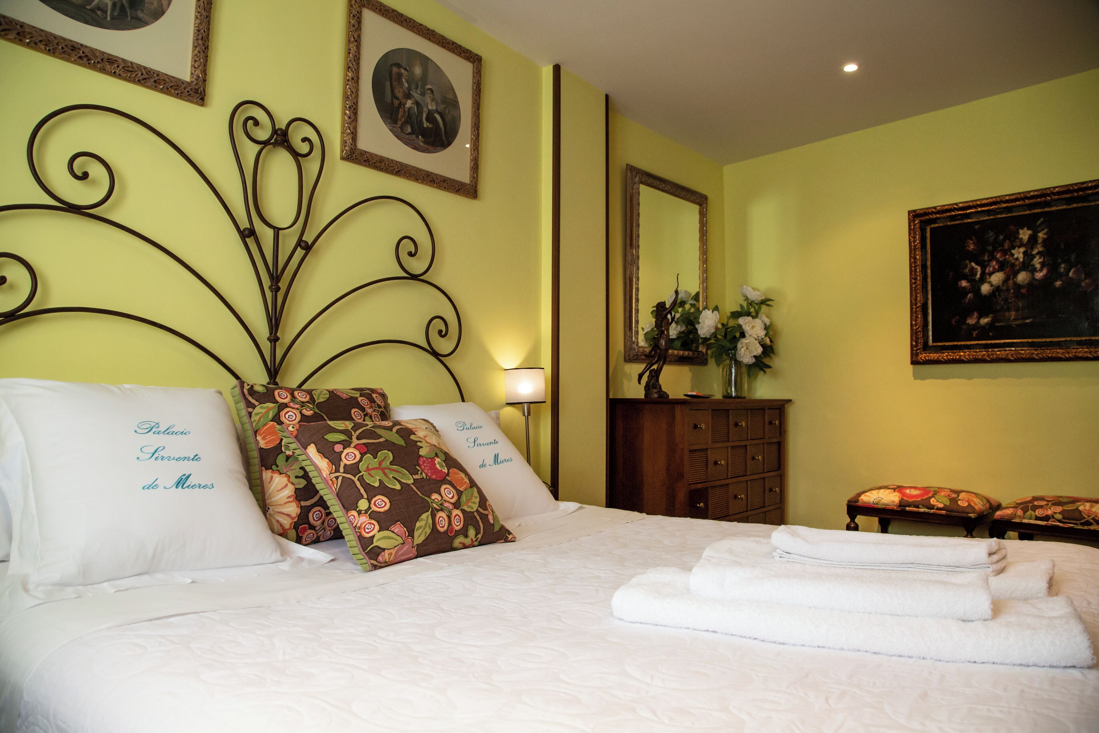 A neatly made bed with pillows, a bedside table with a vase, and a mirror on the wall.