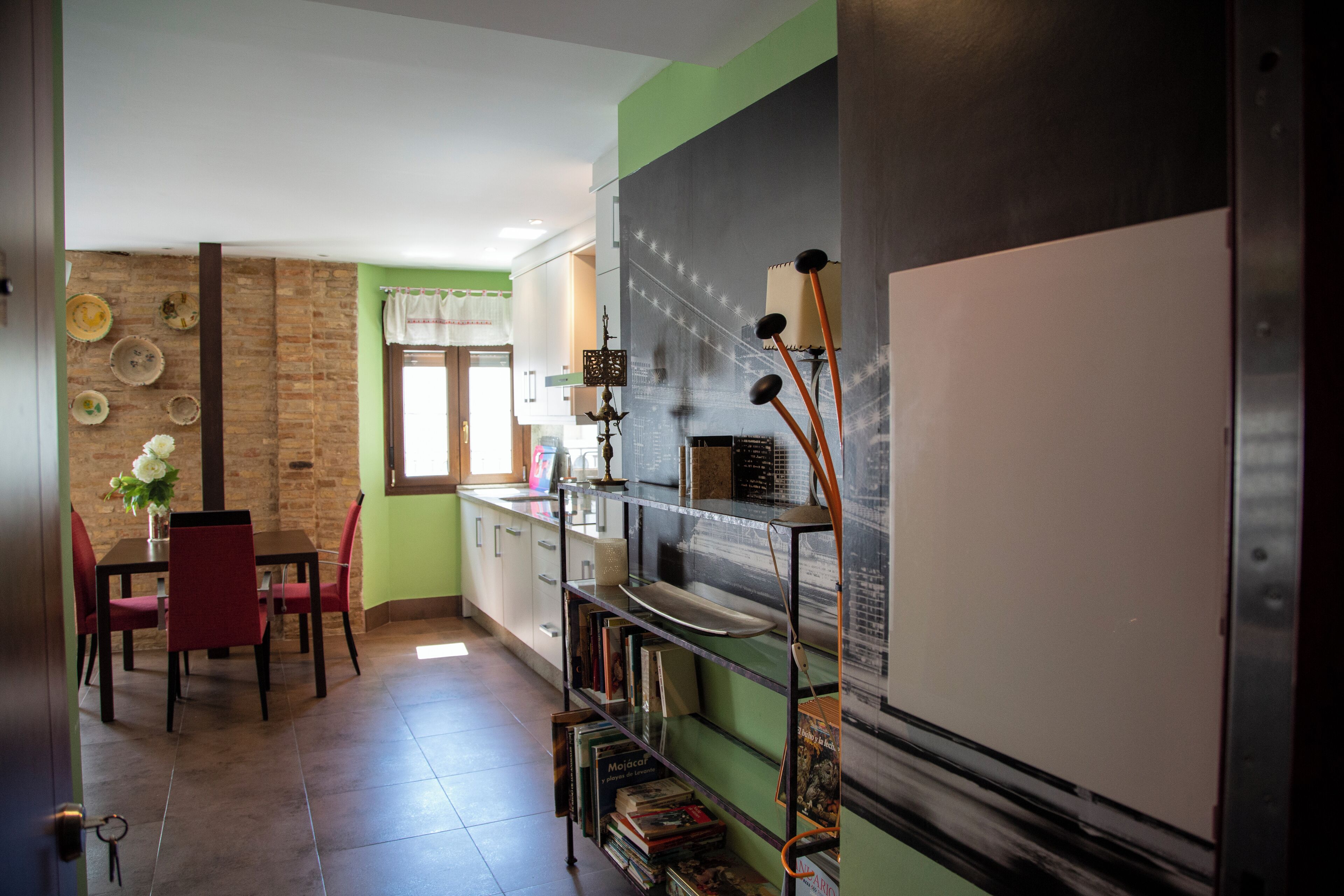 Una cocina con comedor, que presenta una pared de ladrillo, armarios verdes y una estantería.