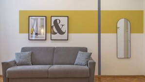 A neutral-colored sofa with two pillows, a framed artwork above it, and a mirror on the wall.