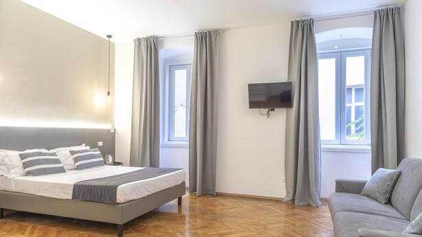 A bedroom with a bed, a sofa, a TV, and two windows with curtains.