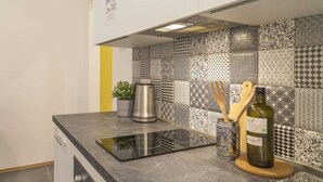 A kitchen with a black induction cooktop, a stainless steel kettle, a potted plant, a bottle of olive oil, and a wooden cutting board.
