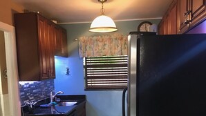 A compact kitchen with dark wooden cabinets, a black refrigerator, a built-in oven, a sink, and a window with blinds.