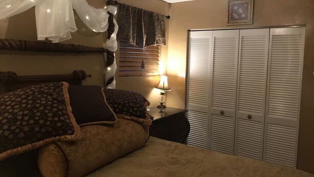 A bedroom with a bed, a nightstand, a lamp, a wardrobe, and a ceiling fan.