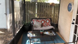 A covered patio with a cushioned seating area, a small table, and a potted plant.