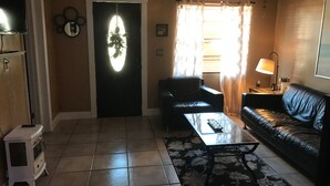 A living room with a black leather sofa, a glass coffee table, and a patterned rug.