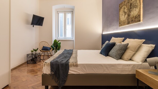 Une chambre à coucher comprenant un lit, un téléviseur à écran plat, une fenêtre, une plante et une œuvre d’art accrochée au mur.