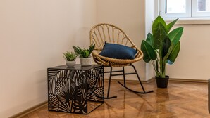 Une pièce comprenant un fauteuil en osier, une petite table au motif géométrique et une plante en pot.
