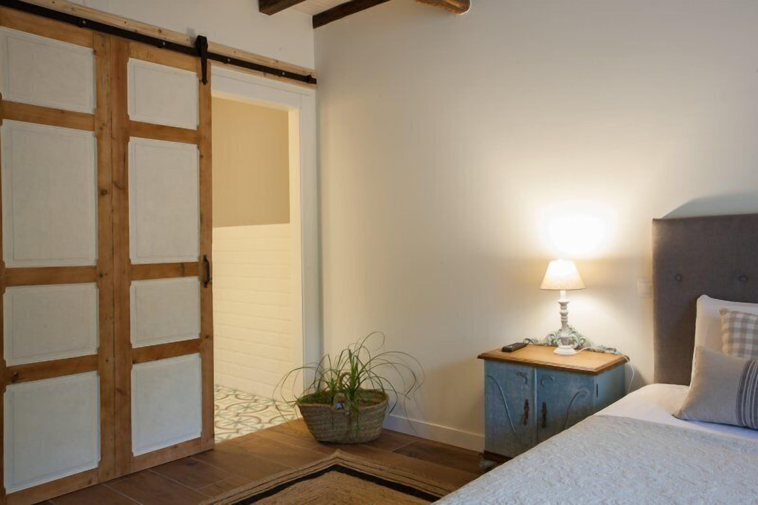 A bedroom with a bed, a nightstand with a lamp, a sliding door, and a potted plant.